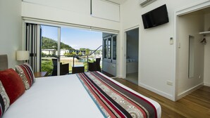 A hotel room with a large bed, a TV mounted on the wall, and a balcony with a view of the surrounding area. - Beachside Apartment 13 (Nelly Bay)