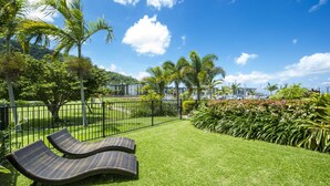 A well-maintained lawn with two lounge chairs, a metal fence, and a view of a marina with boats. - Beachside Apartment 13 (Nelly Bay)