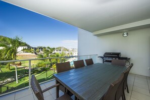 Een balkon met een eettafel en stoelen, een barbecue en uitzicht op een jachthaven en gebouwen.
