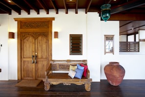 Una porta di legno finemente intagliata, una panca con cuscini, un vaso di terracotta grande e un recinto di legno sullo sfondo.