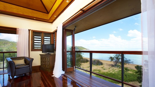 A spacious balcony with a wooden floor, a television, and a view of the beach and ocean. - Lotus House (Horseshoe Bay)