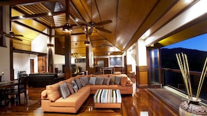 A spacious living area with a large sectional sofa, wooden flooring, ceiling fans, and a view of the outdoors. - Lotus House (Horseshoe Bay)
