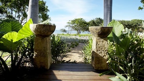 A wooden pathway leading to a beach with palm trees and tropical plants. - Lotus House (Horseshoe Bay)