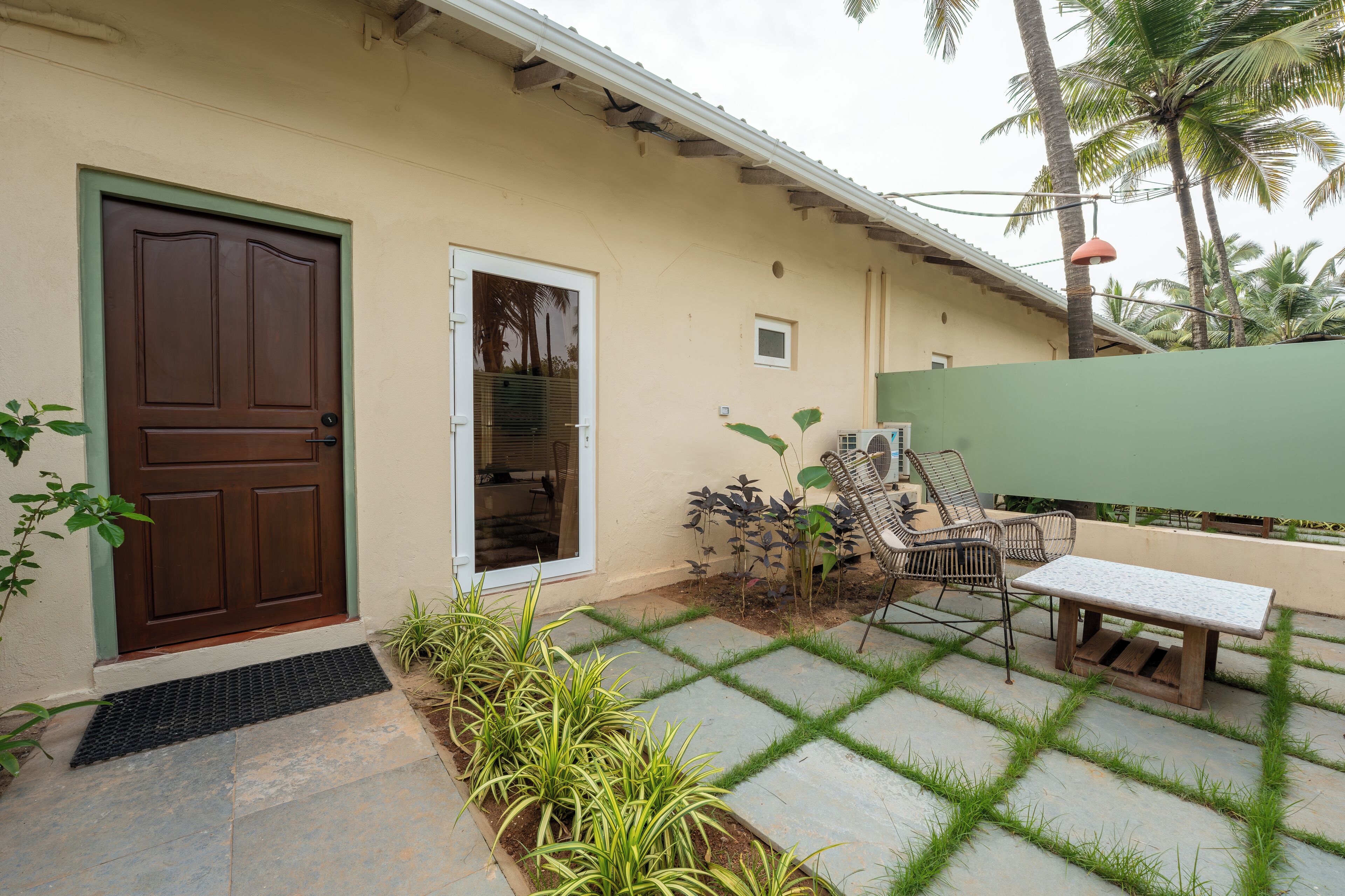Une maison avec une porte marron, une petite fenêtre et un patio avec un banc et des chaises.