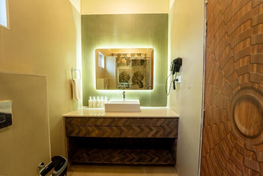 A bathroom with a white sink, a mirror, and a shower. There are toiletries on the sink and a towel rack.