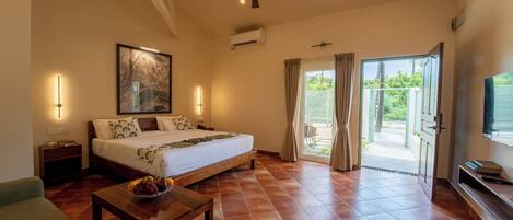 A spacious bedroom with a bed, a ceiling fan, a nightstand, a bedside table with a fruit bowl, and a view of the outside through a sliding glass door.