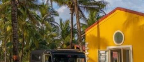 A black off-road vehicle parked in front of a yellow building with a white fence, surrounded by palm trees.