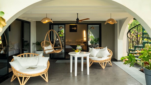 A modern interior with wicker furniture, a ceiling fan, and a view of a lush garden through an arched doorway. - C'Roque Beach Resort (Colva)