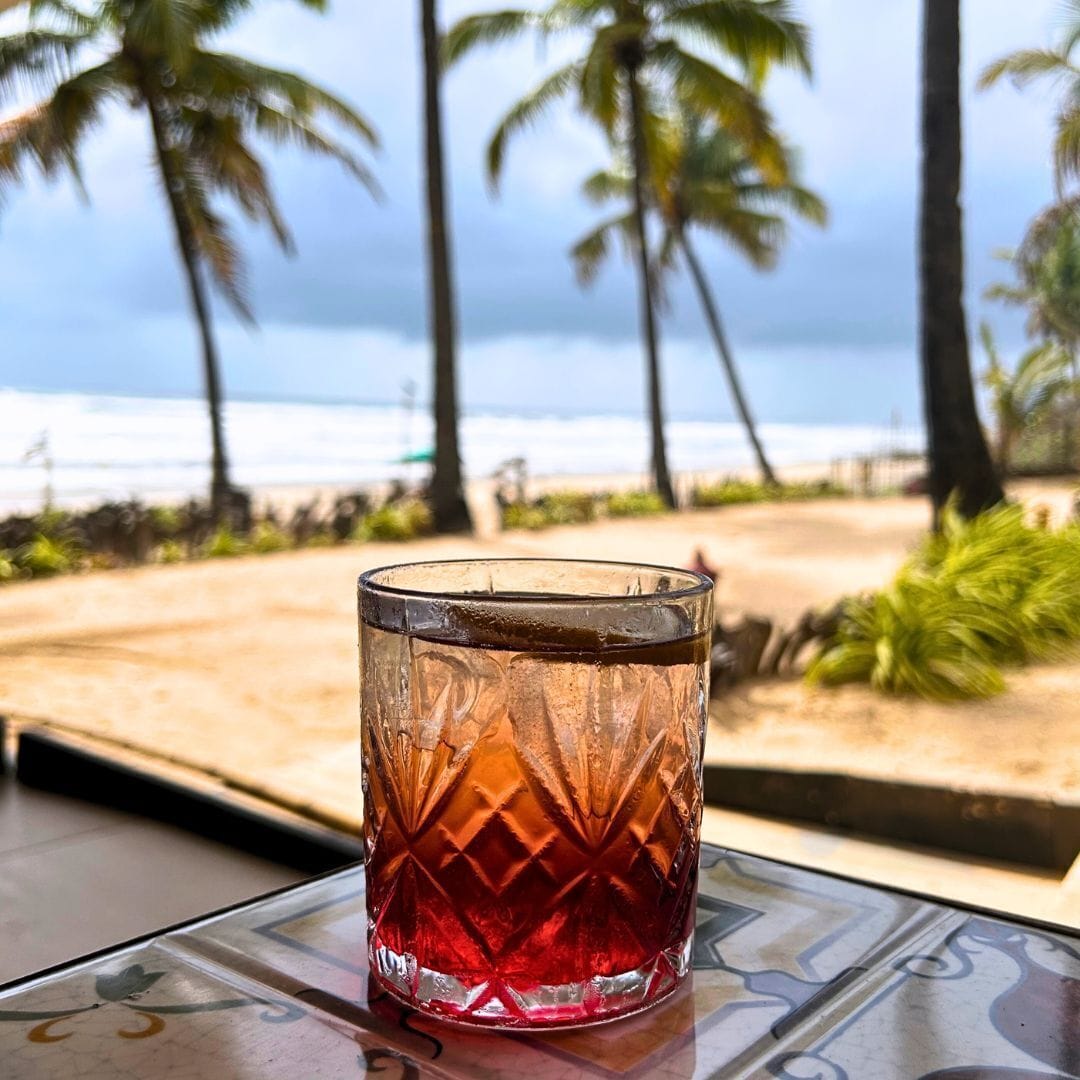 A glass with a textured pattern on a table with a view of the beach and palm trees.