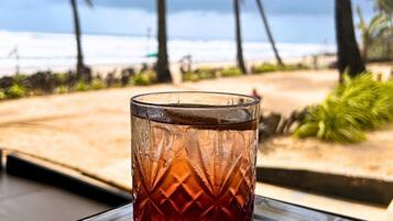 A glass with a textured pattern on a table with a view of the beach and palm trees.