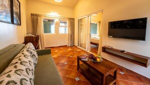 A living room with a sofa, a coffee table with fruit, a TV, and a sliding glass door leading to a balcony. - C'Roque Beach Resort (Colva)