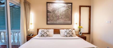 Una habitación de hotel con una cama grande, una mesita de noche con lámpara, una obra de arte enmarcada sobre la cama y vistas al exterior a través de la ventana.