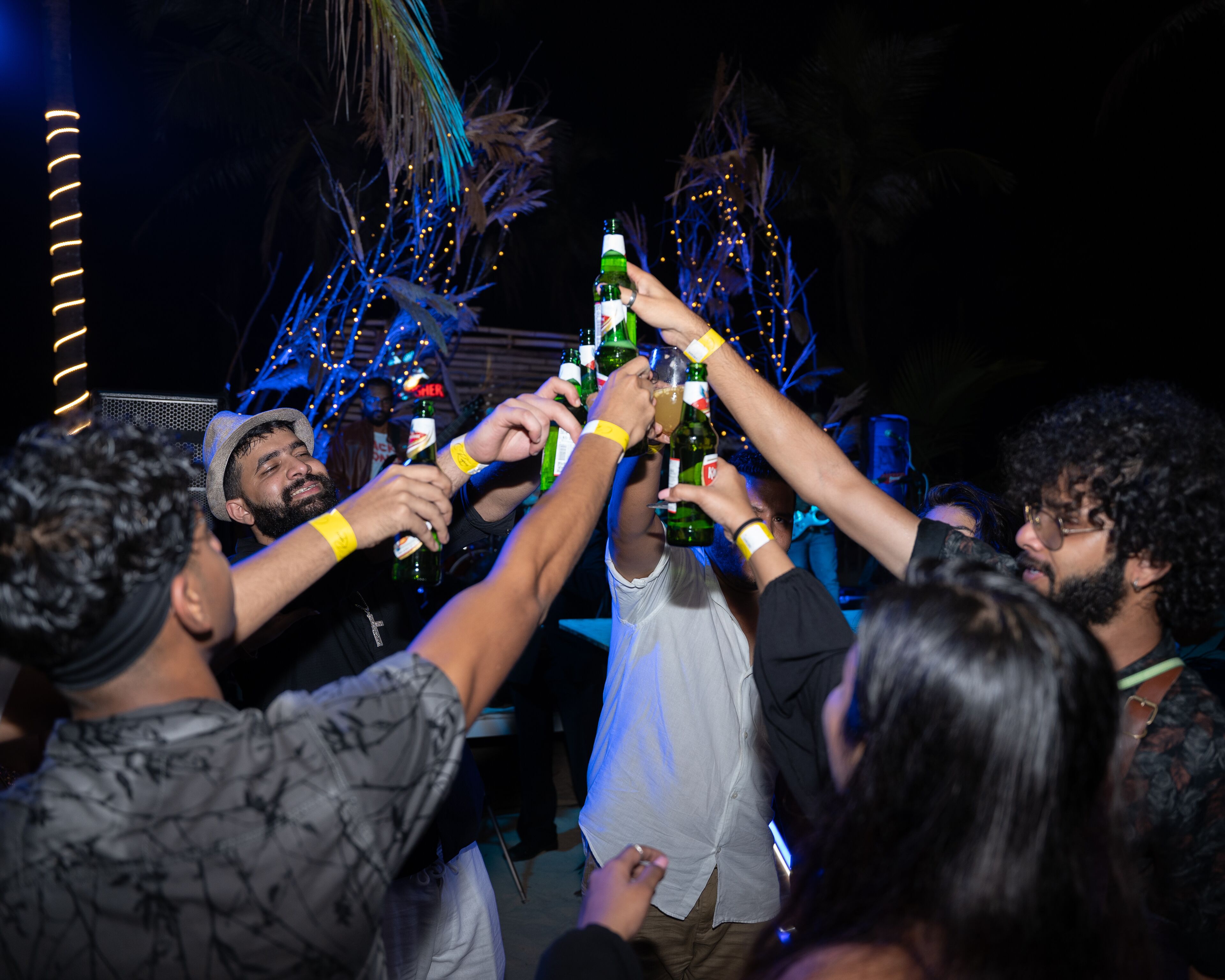 Un grupo de personas brindando con botellas en un ambiente interior tenuemente iluminado.