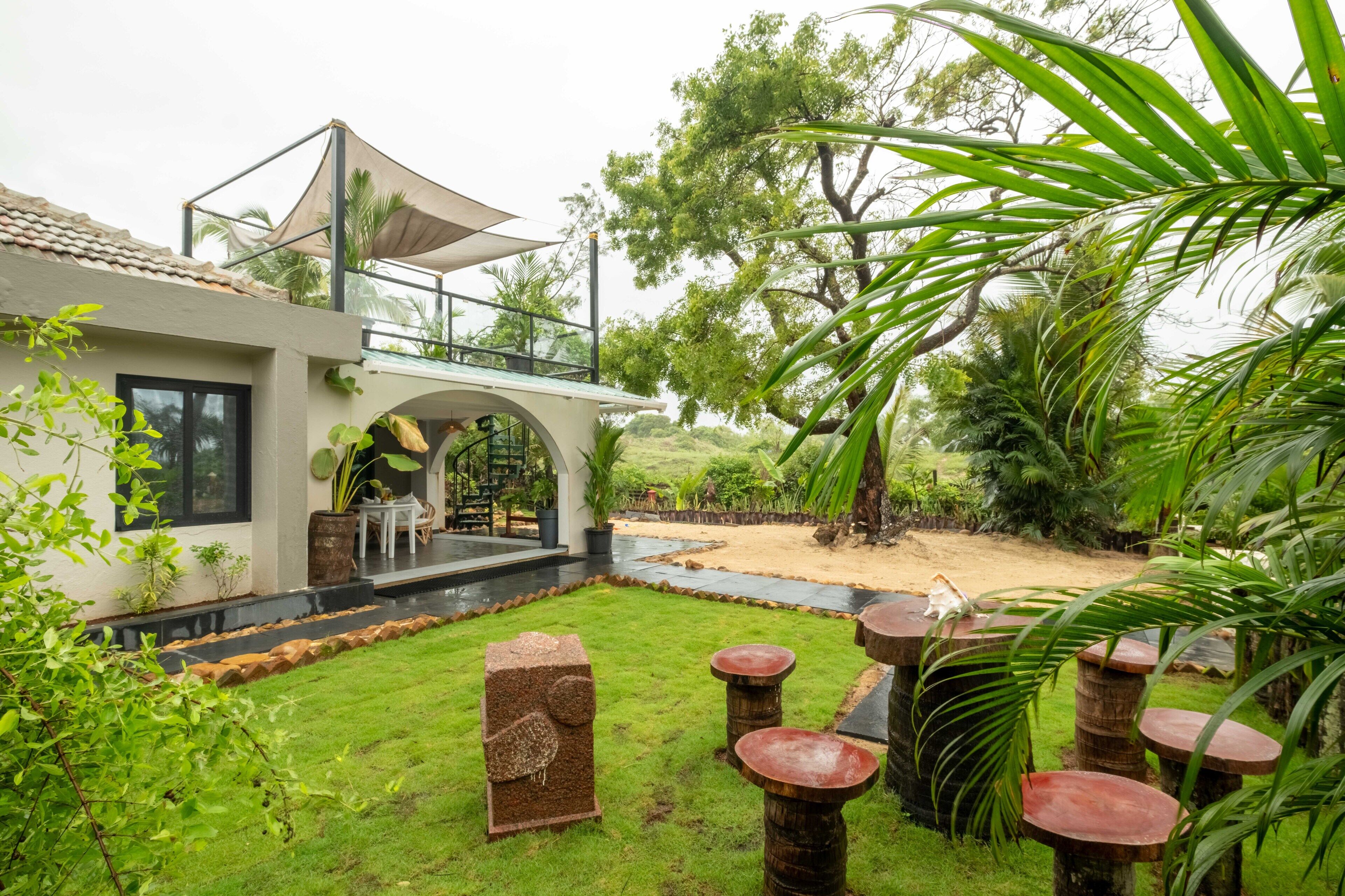 A modern house with a covered outdoor area, a patio with a table and chairs, and a garden with palm trees.