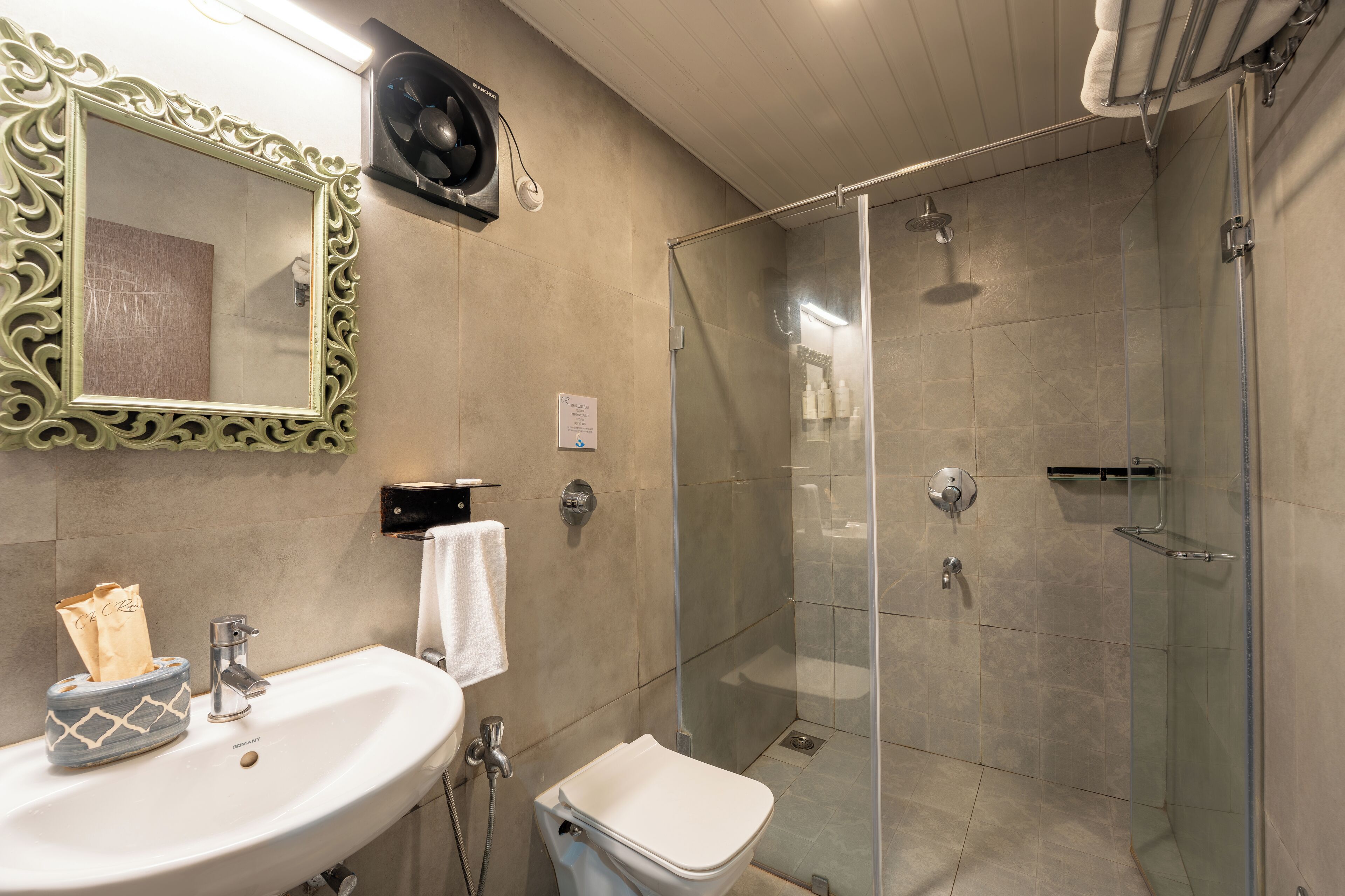 A bathroom with a glass-enclosed shower, a sink with a towel, and a decorative mirror.