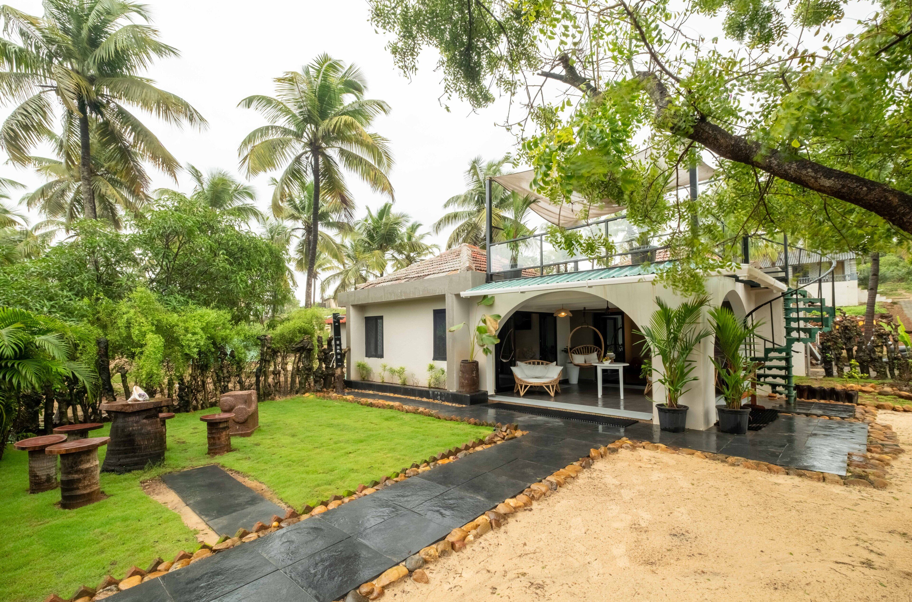 A house with a covered porch, a staircase, and a garden with palm trees.