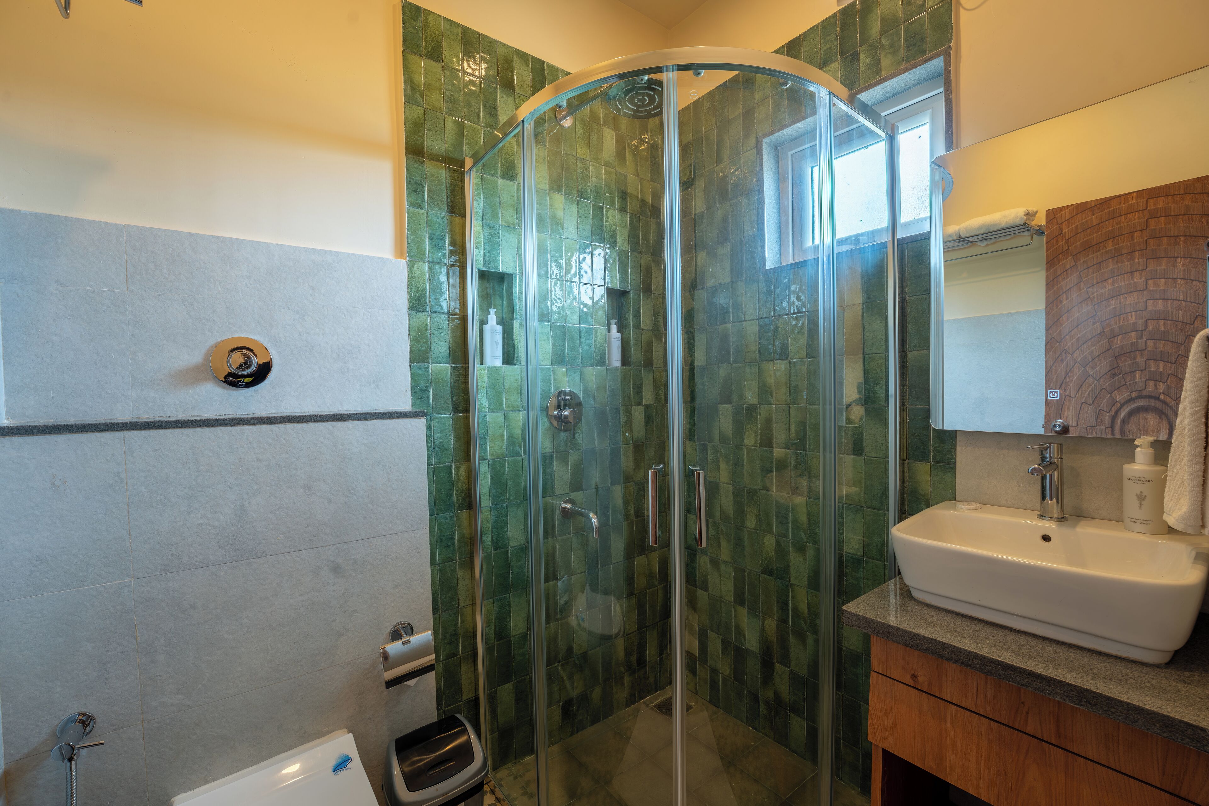 Un bagno moderno con doccia vetro, lavandino bianco e mobile contenitore in legno.