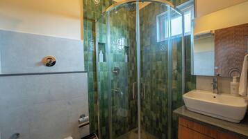 Un bagno moderno con doccia vetro, lavandino bianco e mobile contenitore in legno.