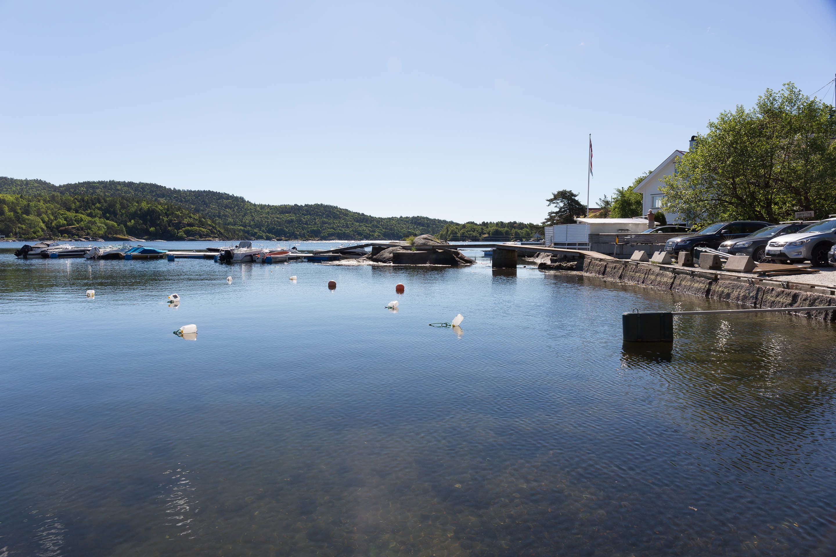 A calm lake with boats docked on the shore, surrounded by trees and hills.