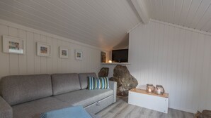 A modern living room with a grey sectional sofa, a white bench, and a mounted TV. - Soltvedts Cabin - Bjønnes (Porsgrunn)