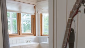 A room with a wooden floor, white walls, a window with blinds, and a guitar leaning against the wall. - Soltvedts Cabin - Bjønnes (Porsgrunn)