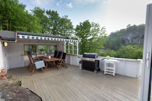 Una terraza con mesa y sillas, una parrilla y vistas de la vegetación circundante.