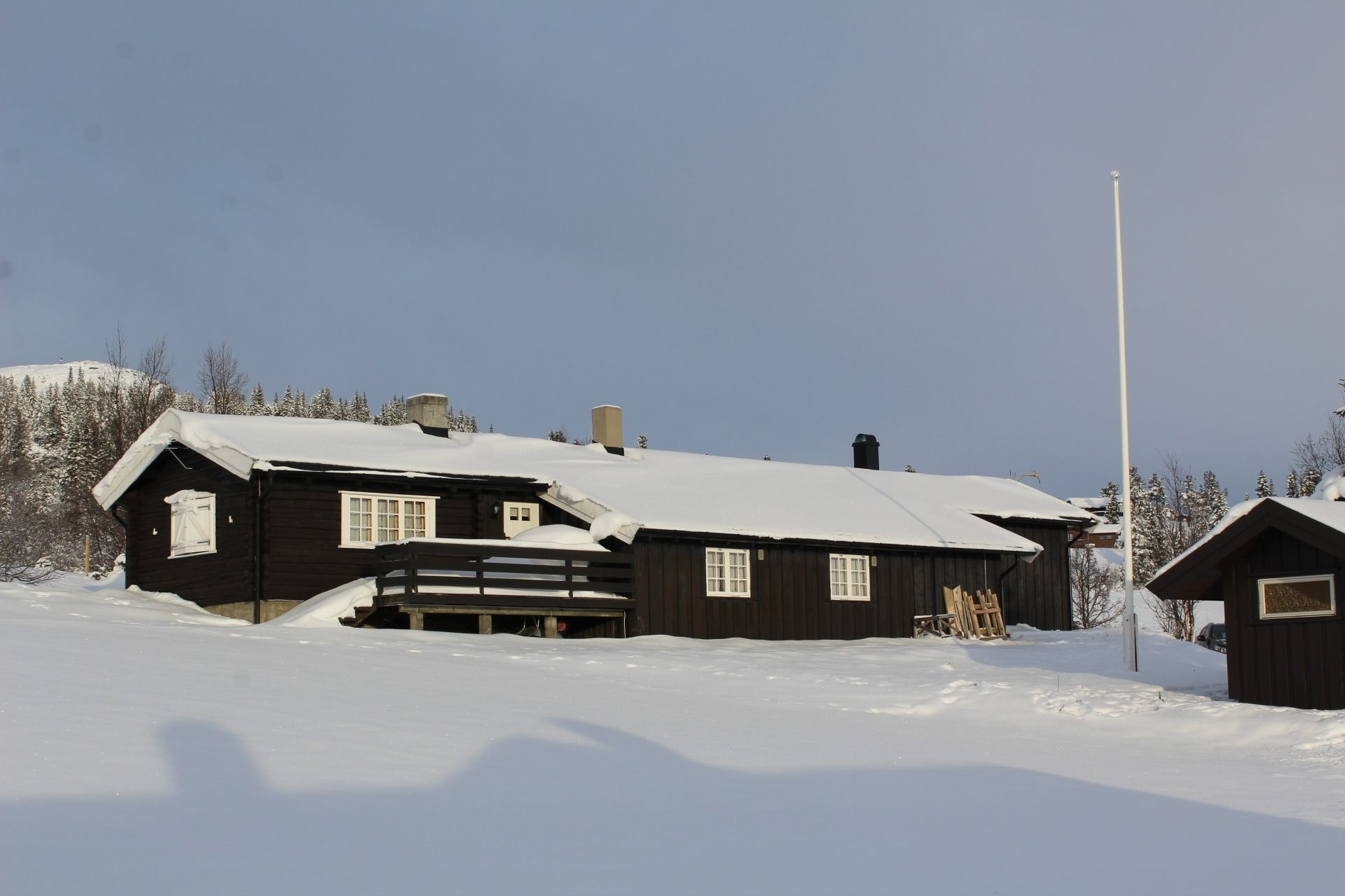 Une cabane en bois avec un toit enneigé, une clôture en bois et un ciel dégagé.
