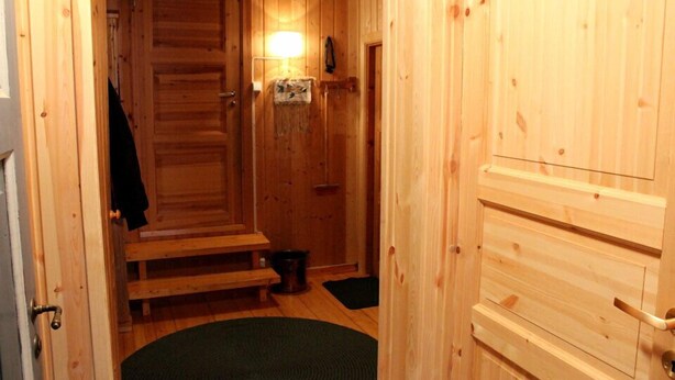 A wooden interior hallway with a door, a bench, a trash bin, and a small rug.