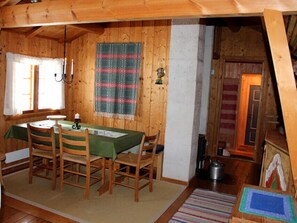 A cozy wooden dining room with a table set for four, a hanging tapestry, and a view into another room with a stove. - Lilleset Cabin - Gol (Gol)