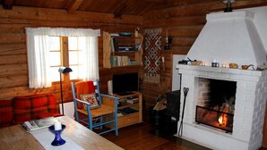 A cozy log cabin interior with a fireplace, wooden furniture, and a bookshelf.