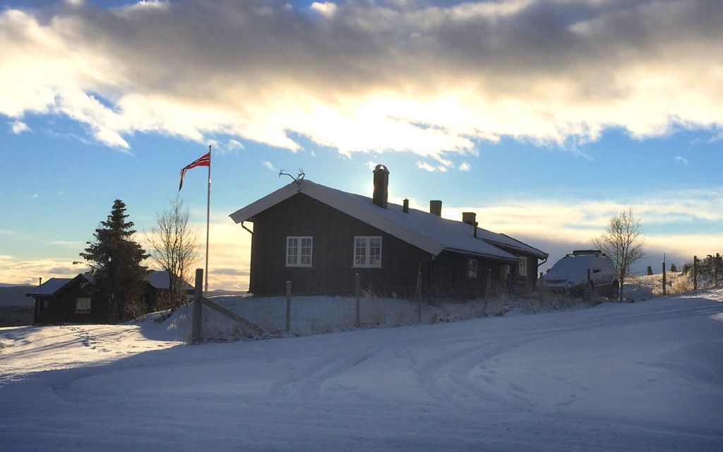 A wooden cabin with a snow-covered roof, a flagpole with a flag, and a clear sky.
