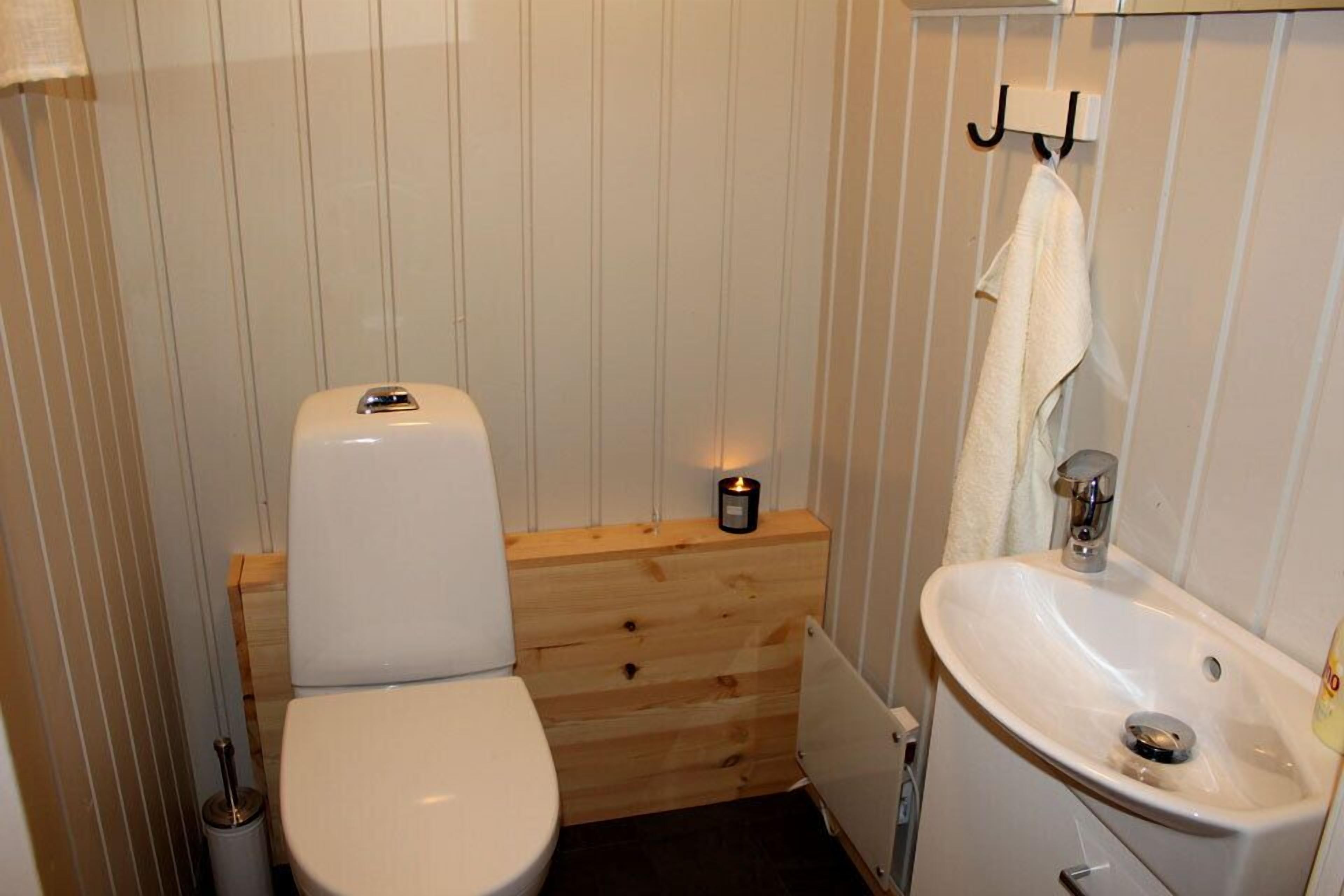 Une petite salle de bain compacte avec des toilettes blanches, un meuble-lavabo en bois et un lavabo blanc.