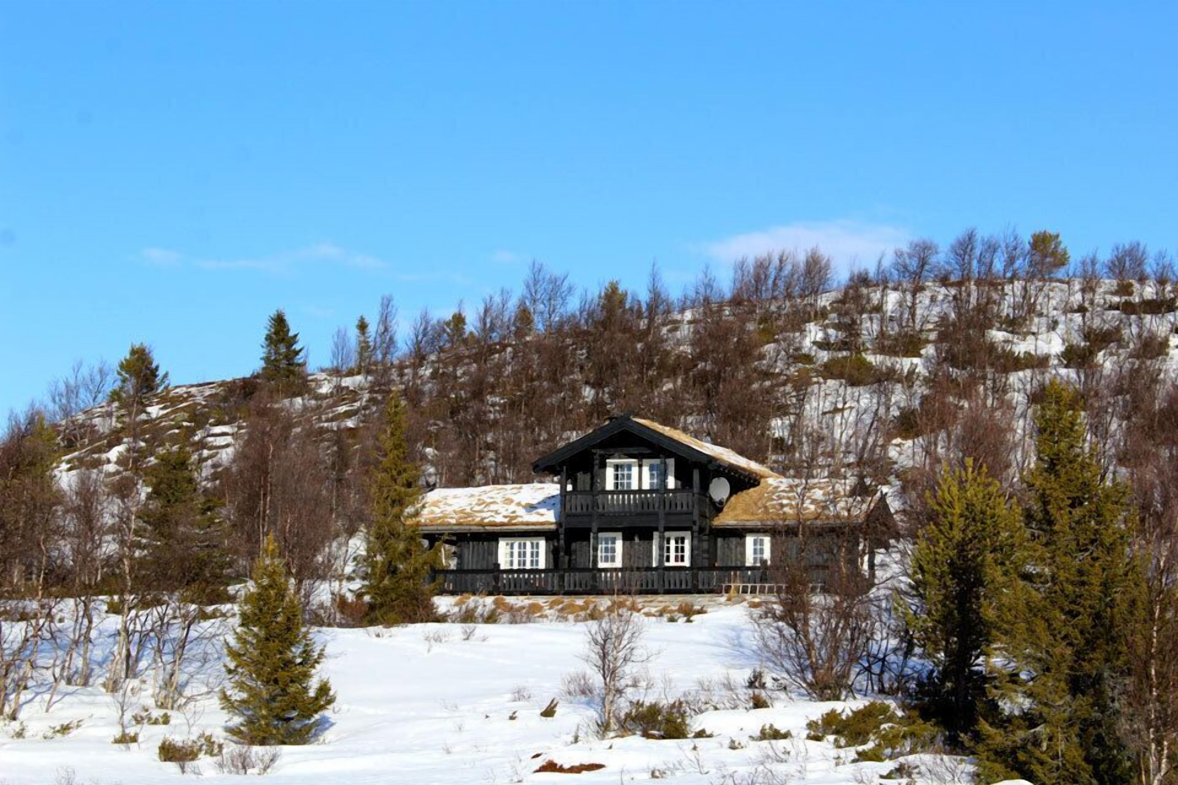 A wooden cabin with a balcony, surrounded by snow and trees.