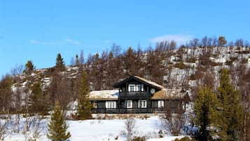 A wooden cabin with a balcony, surrounded by snow and trees.