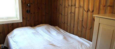 A small, single-bed room with wooden panel walls, a window, and a white bedspread.