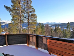 A wooden deck with a view of snow-capped mountains and pine trees. - Heibu Cabin - Skåbu (Nord-Fron)
