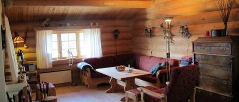 Un acogedor interior de cabaña de madera con techo de madera, un sofá, una mesa de comedor y un aparador.