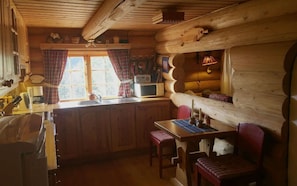 A cozy cabin interior with wooden walls, a kitchen area with a microwave, and a dining table with chairs. - Heibu Cabin - Skåbu (Nord-Fron)