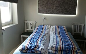 A bedroom with a bed, two chairs, a window, and a wall-mounted light. - Haver Cabin - Sirevåg (Ha)