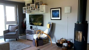 A living room with a TV, bookshelves, a guitar, a fireplace, and a comfortable seating area. - Haver Cabin - Sirevåg (Ha)