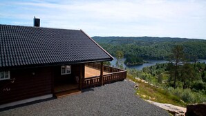 Una cabaña con terraza de madera y vistas a un lago y bosque.