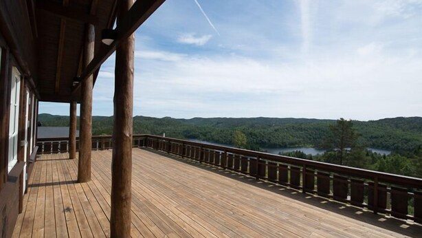 Una terraza de madera con barandilla que da a un paisaje boscoso y un lago.