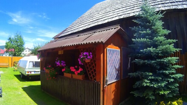 A wooden cabin with a corrugated metal roof, a wooden fence, and a small garden area with pink flowers. - Apartments Majercak (Zuberec)