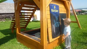 A wooden playhouse with a Martiner logo, a slide, and a small window. - Apartments Majercak (Zuberec)