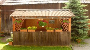 A wooden structure with a corrugated metal roof, featuring multiple flower planters and a small table. - Apartments Majercak (Zuberec)