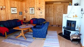 Ein Holzblockhaus-Interieur mit einer Sofaecke, einem kleinen Tisch, einem Kamin und Wandlampen.