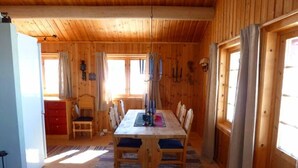 Ein Holzblockbau-Innenraum mit Esstisch, Stühlen, einem roten Schrank und einem Fenster mit Vorhängen.
