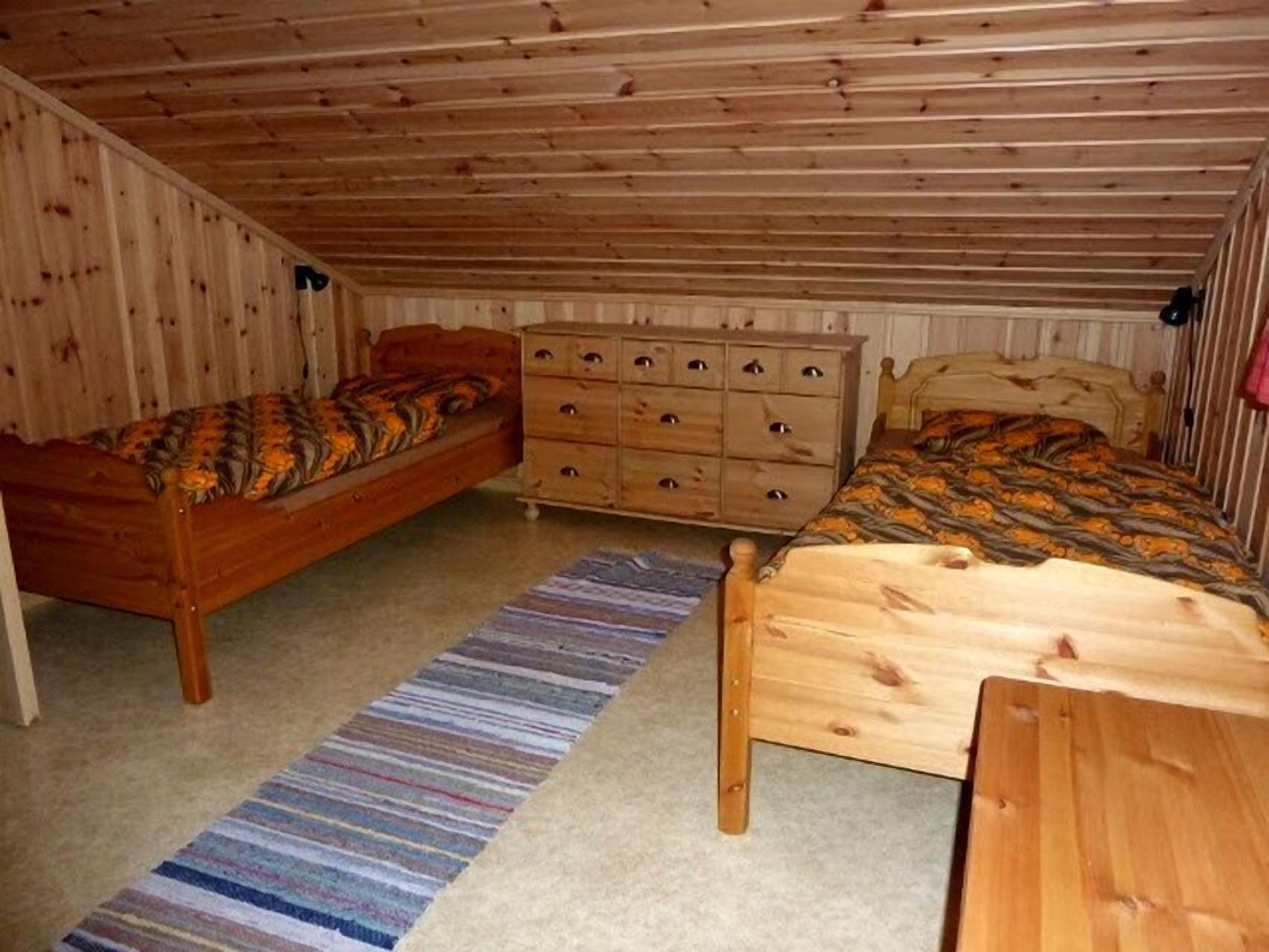 A small, wooden-paneled attic bedroom with two single beds, a dresser, and a striped rug.