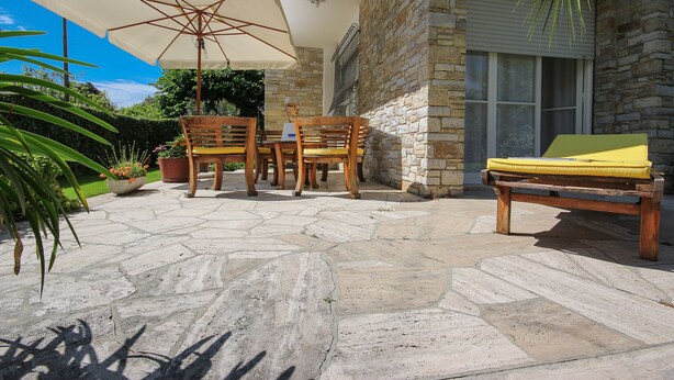 An outdoor patio with stone flooring, wooden furniture, and a large umbrella. - B&B Ortensia (Forte dei Marmi)