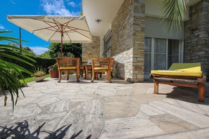 Un patio exterior con suelo de piedra, mobiliario de madera y una sombrilla grande.